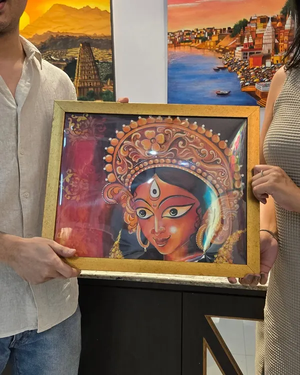 A collector holds a newly purchased, beautifully framed painting of the goddess Durga by artist Simran, a piece from our "Vernissage" exhibition.