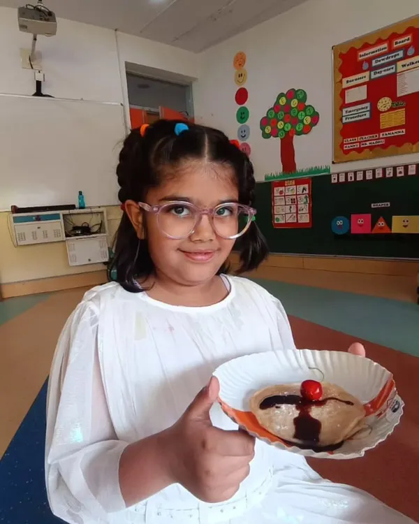 Our culinary arts program is a camp favorite, where children learn basic cooking skills and kitchen safety. This young chef proudly presents her chocolate-drizzled pancake, a delicious result of a hands-on session that combines creativity with practical life skills.
