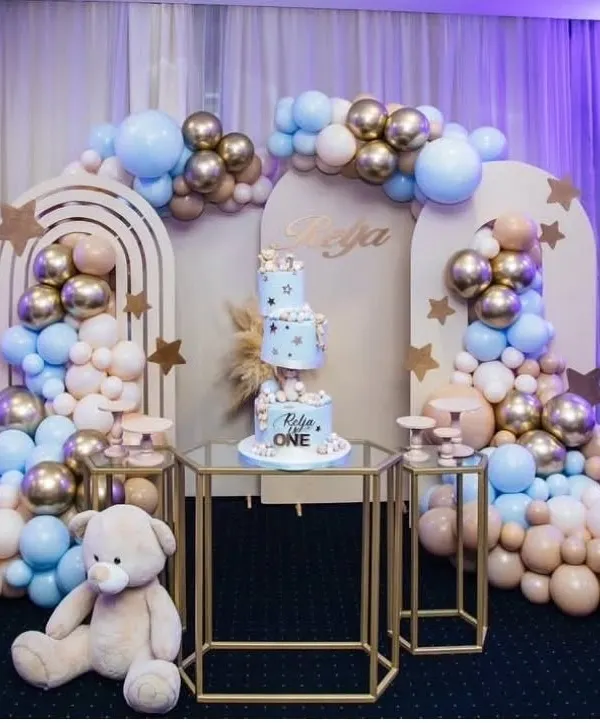We designed this elegant teddy bear themed first birthday with a sophisticated pastel blue, beige, and gold color palette. The complete setup includes custom arched backdrops, a multi-tiered cake display, and cascading balloon arrangements for a modern and chic celebration.