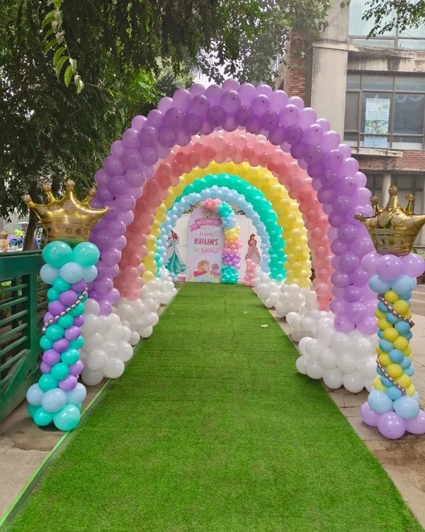 A spectacular rainbow balloon arch creating a magical tunnel entrance for a princess party on a green lawn.