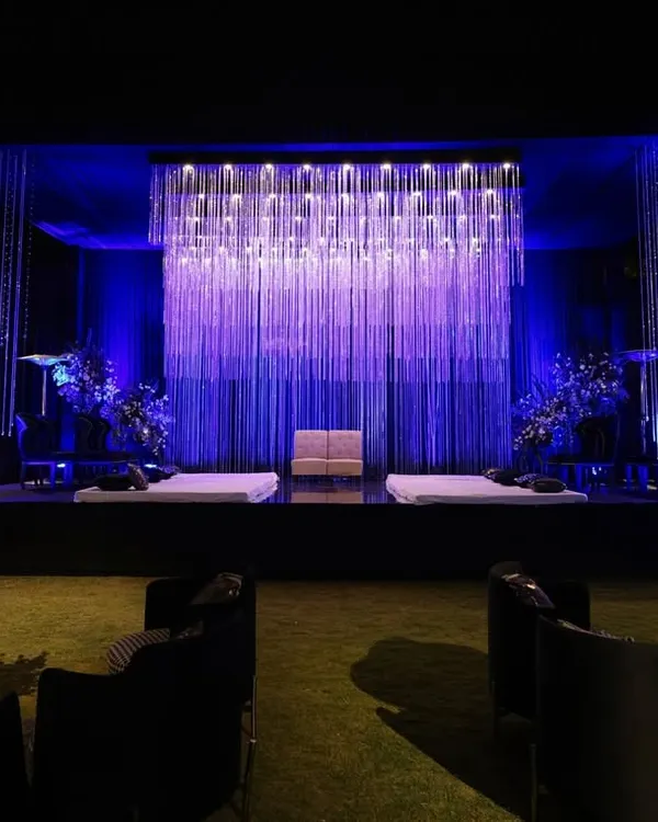 I designed this sangeet stage with a waterfall of shimmering crystal strings under deep blue light, creating a backdrop that was both regal and romantic for an evening of performances.