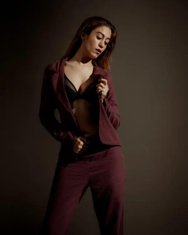 A moody, low-key portrait focusing on form and texture. The lighting is shaped to highlight the model's pose and the fabric of the suit, creating a sense of quiet confidence.