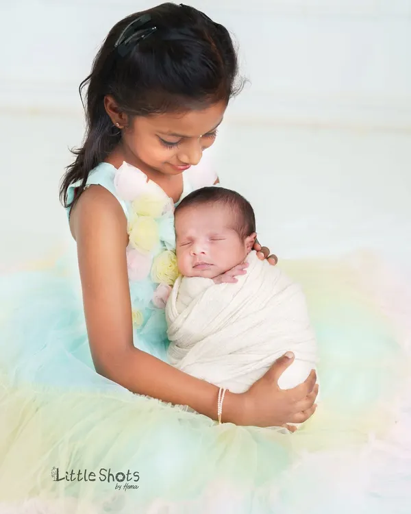 A big sister looks down with so much love at her sleeping newborn sibling. The pastel colors of her dress add a soft, dreamy feel to this incredibly sweet moment.