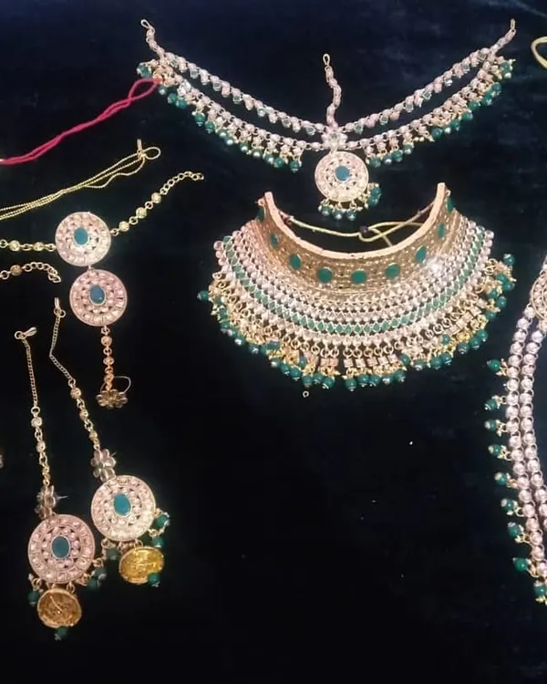 This is the quintessential grand bridal jewellery set, available for rent. It includes a gold-finish choker and a matching multi-layered rani haar, both studded with green stones, along with a maang tikka, hathphool, nath, and earrings to give you a complete, regal look for your wedding day.