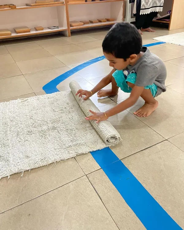 The day begins with choosing a workspace. A child carefully unrolls his mat, an important Montessori exercise that defines his personal area and teaches respect for his own work and the work of others.