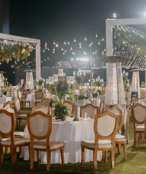 A magical dinner setting under the stars. We used hanging greenery, Edison bulbs, and elegant white table settings to create a 'Luxe Garden' reception that felt both grand and romantic.
