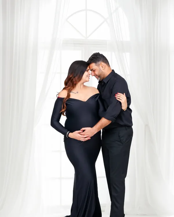 An intimate studio portrait of an expecting couple sharing a quiet moment, their foreheads touching. The soft lighting and their coordinated black outfits create a feeling of timeless elegance and deep connection.