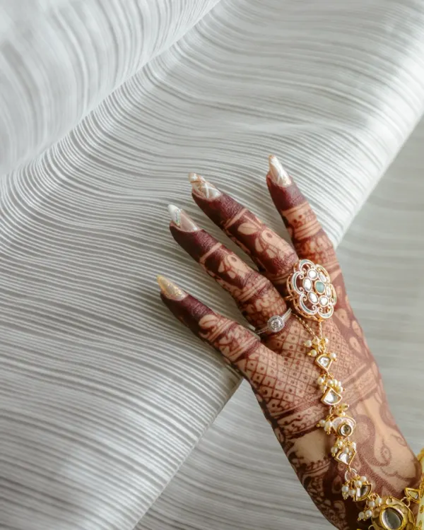A close-up shot of the bride's hand, showcasing the intricate mehendi design and a beautiful traditional hathphool.
