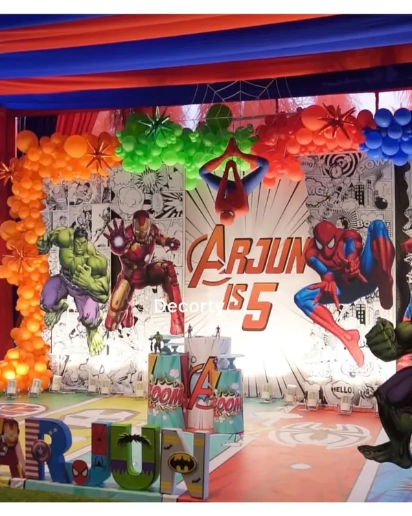 An explosive Avengers-themed stage backdrop for Arjun's 5th birthday. It features a comic-book style background, character cutouts, and personalized 3D letters.