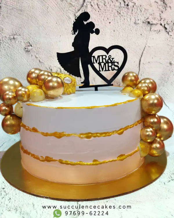A beautiful and elegant cake to celebrate a new chapter as Mr. & Mrs. The design features a soft pink and white ombre effect with gold accents and is topped with a silhouette of the couple, perfect for an engagement or anniversary.