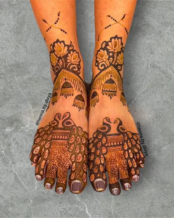 A stunning bridal feet design featuring majestic peacocks. The intricate feather patterns flow beautifully down the feet, complemented by lotus and jhumka details for a royal look.