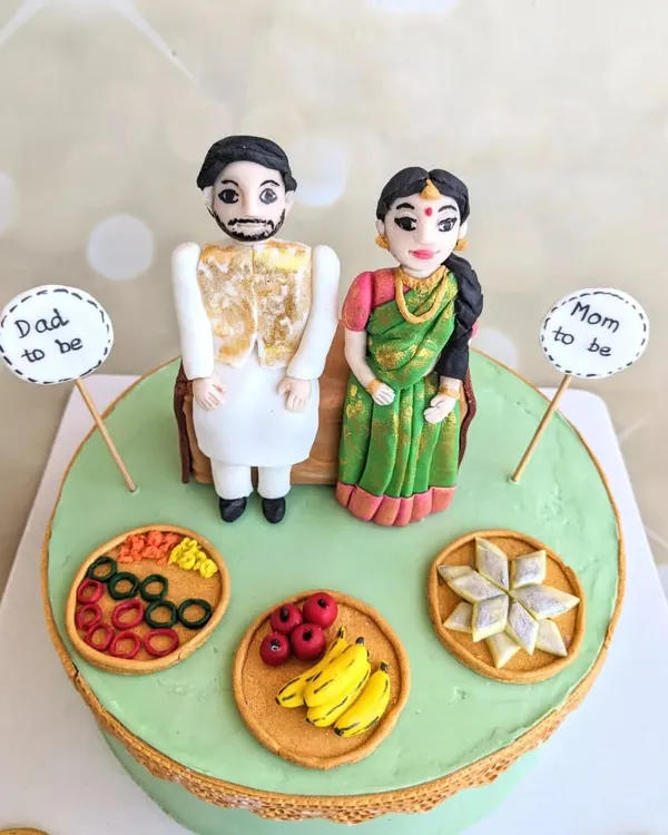 This traditional baby shower cake was a joy to create. It features handcrafted fondant toppers of the parents-to-be, along with miniature plates of traditional sweets and fruits.