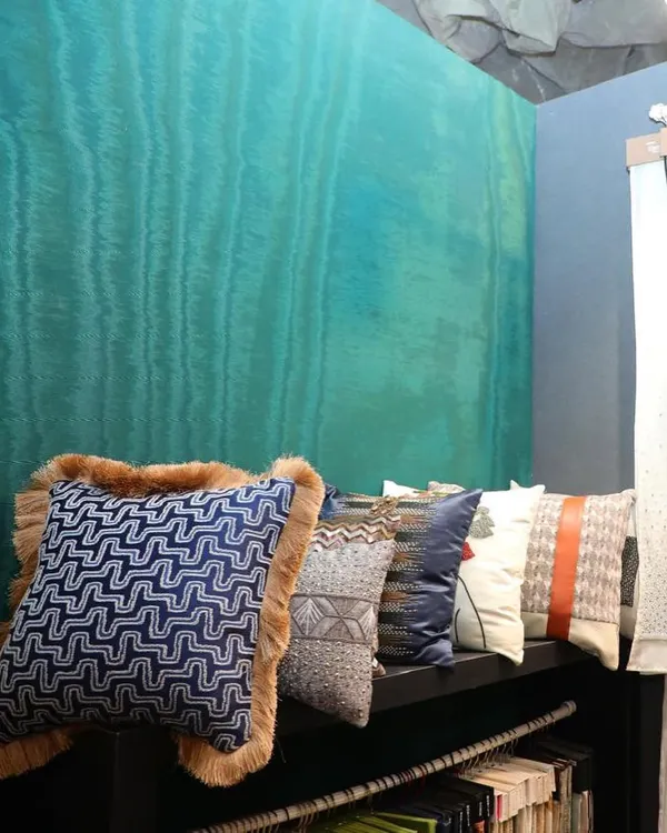 A row of our exquisite cushions, featuring a variety of textures from intricate beading to plush fur trim, set against a vibrant turquoise wallcovering. This showcases how our fabrics and wallpapers can be coordinated to create a rich, layered look.