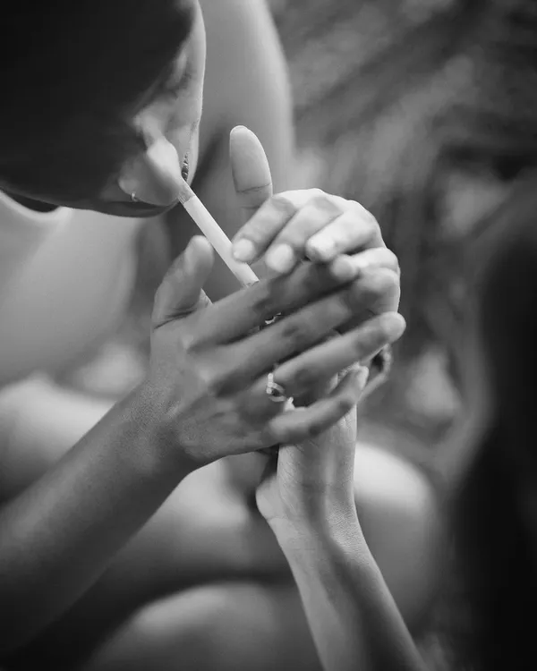 An intimate black and white close-up of two people sharing a moment, with one lighting a cigarette for the other. The focus on their hands creates a raw and personal narrative.