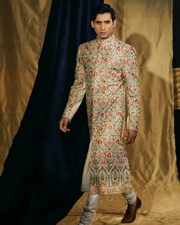 A kingly statement. This cotton silk sherwani is fully adorned with intricate multi-color Resham work, creating a wearable piece of art for your wedding day.