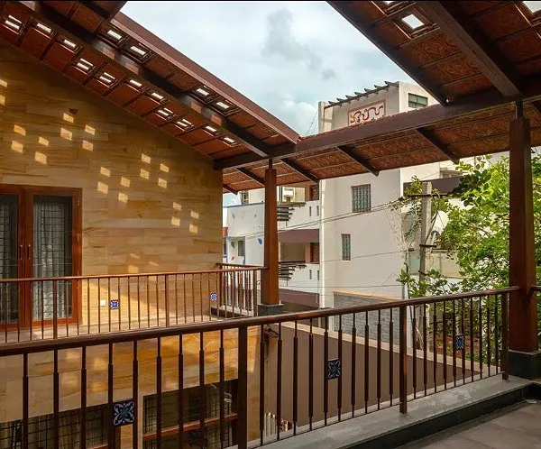 The upper-level veranda at Nivriti, Chatty’s House, overlooks a central open space, creating connectivity between different parts of the home. The perforated roof design allows dappled sunlight to filter through, creating dynamic light patterns.