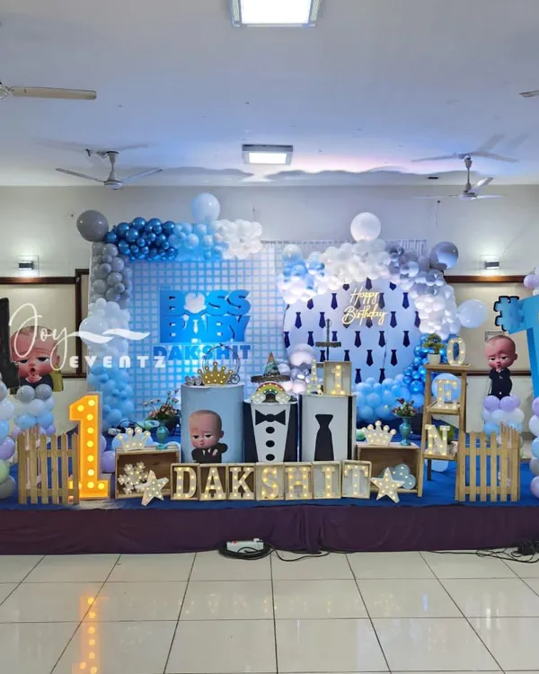 This is a complete Boss Baby themed stage I created for a first birthday party. The setup includes a custom grid backdrop, multiple character cutouts, themed plinths for the cake, illuminated marquee letters for the name, and a large light-up number '1'.