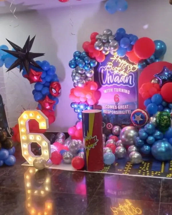 An action-packed Avengers theme for a 6th birthday. This setup includes a large backdrop, marquee number, character cutouts like Batman and Spider-Man, and a balloon arrangement in superhero colors.