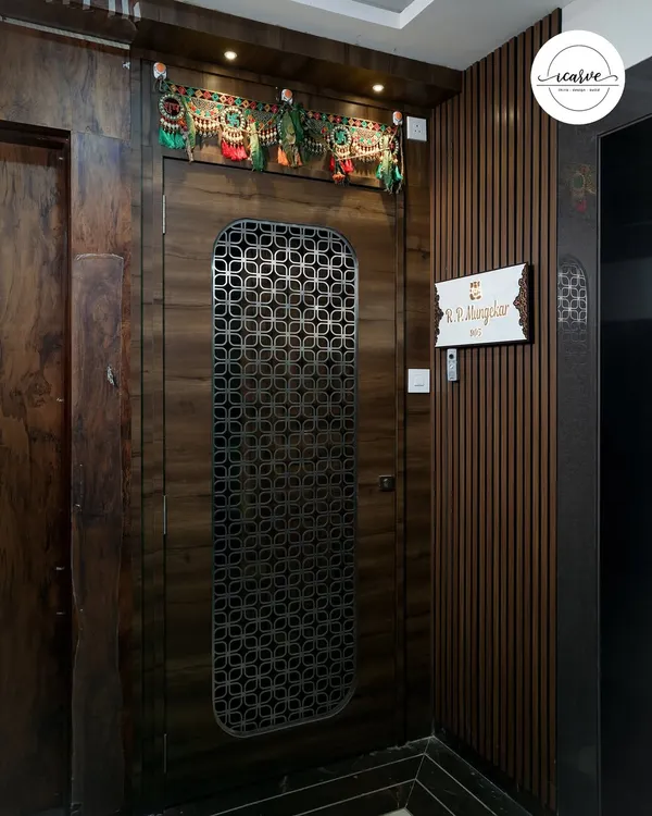 A statement entrance featuring a main door with a custom geometric metal grill. The surrounding wall is clad in dark wood paneling, creating a rich and sophisticated welcome.