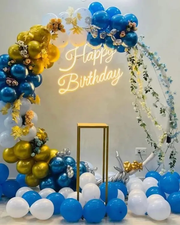 A classic and clean balloon arch design perfect for any celebration. This setup features a mix of blue, gold, and white balloons, with a warm 'Happy Birthday' neon sign at the center. It's a versatile backdrop that works well in many spaces.