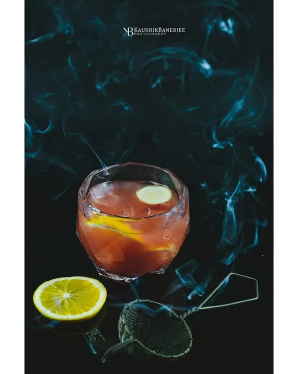 A smoky citrus cocktail against a dark, moody background. I use techniques like smoke to add drama and atmosphere, creating an alluring image for a bar's specialty drink menu.