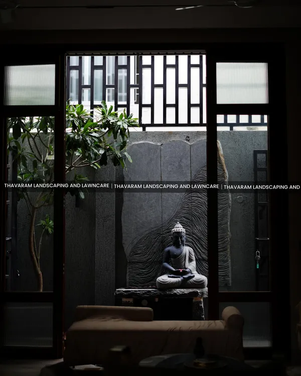 A view from indoors looking out into a tranquil courtyard we designed. A meditative Buddha statue sits as the centerpiece, framed by glass doors and complemented by a single tree, creating a perfect picture of serenity.