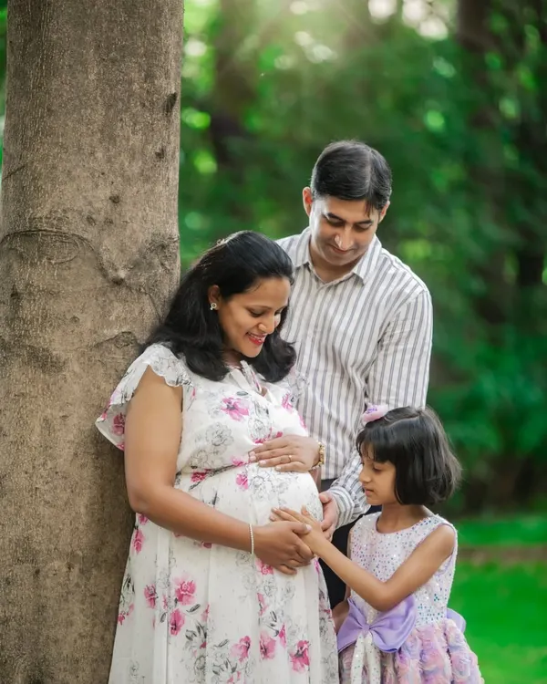 A heartwarming family moment where the older sister gently touches her mother's baby bump, with the father looking on lovingly.
