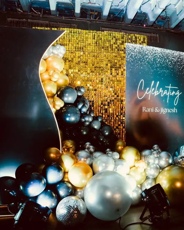 A modern and glamorous backdrop for Rani and Jignesh's celebration. The gold sequin wall provides a sparkling background, while the organic balloon garland in black, gold, and silver adds a touch of modern elegance.