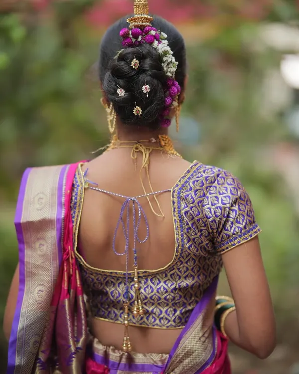 A detailed look at a traditional Maharashtrian Khopa hairstyle. The bun is decorated with fresh flowers and gold accessories, which is a classic choice for brides.