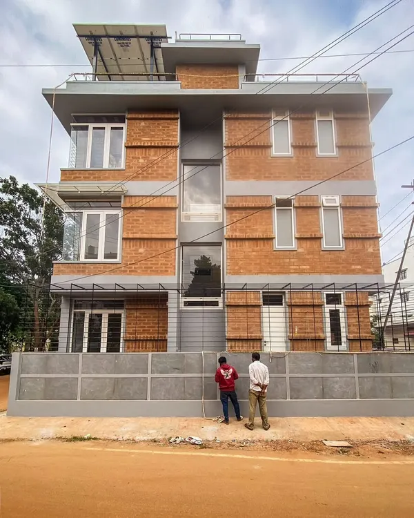 The facade of the Tripathy family home in Bangalore, built upon an existing foundation to minimize waste. The honest, brutalist facade features exposed mud blocks and jaali walls, showcasing our commitment to sustainable urban architecture.