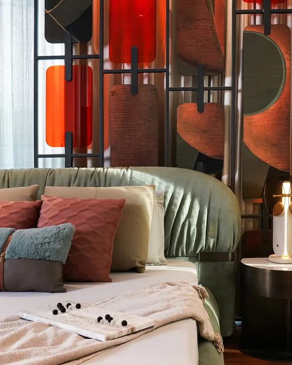 A closer look at the master bedroom's details, including the plush, layered pillows and the elegant side table. The sculptural headboard, with its mix of colors and textures, serves as a stunning piece of art.