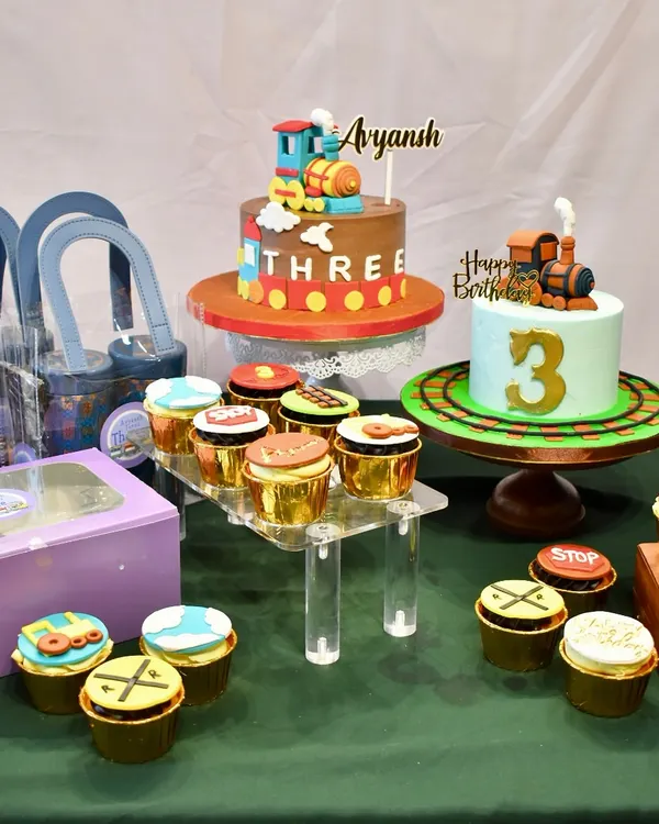 All aboard for a spectacular 3rd birthday. This train-themed dessert table features two custom cakes, dozens of themed cupcakes, and party hampers, creating a complete and cohesive celebration spread.