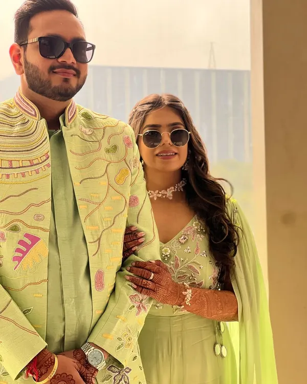 A modern, chic look for a daytime event. We designed this coordinated set in a fresh lime green, featuring a stylish jumpsuit with a cape for her and a matching embroidered sherwani for him.