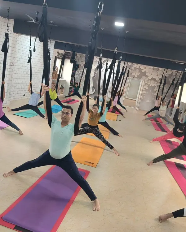 A full class of students exploring aerial yoga, using the hammocks to stretch and strengthen in unison. This is a great way to build community and have fun.