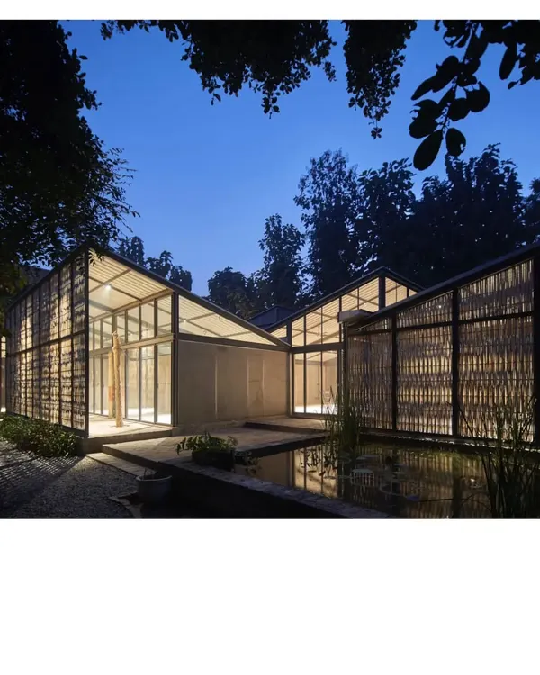 This is the Artist Residency at Farm8 in New Delhi, seen at dusk. The design uses a bamboo exoskeleton to create a series of 'in-between' spaces, allowing the building to breathe and the landscape to flow through. The structure becomes a lantern in the garden, blurring the line between a building and its natural surroundings.