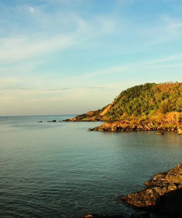 The beautiful coastline of Gokarna at golden hour, showing the rocky shores and green hills that we trek along.