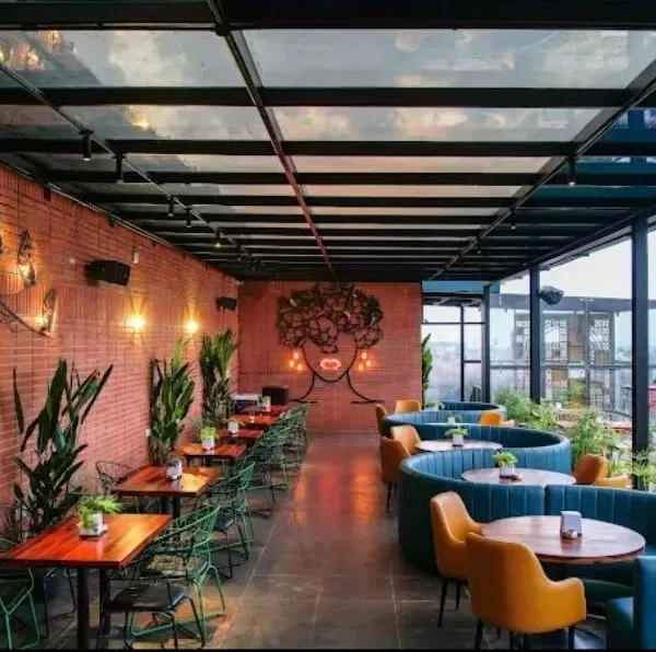 The interior of the Bramble rooftop bar, where we blended landscape and interior design. The space features a glass ceiling, exposed brick walls, and abundant indoor plants, creating a garden-like atmosphere that connects to the open terrace beyond.