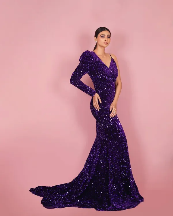 A full-length shot of actress Daisy Shah in a magnificent purple sequined gown. The one-shoulder design and flowing train are captured with studio lighting to emphasize the drama and elegance of the outfit.