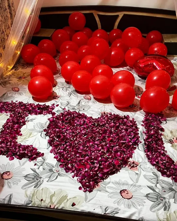 A classic romantic room surprise I set up for an anniversary. This includes a fairy light canopy, red balloons covering the bed, and a personal message spelled out in fresh rose petals.