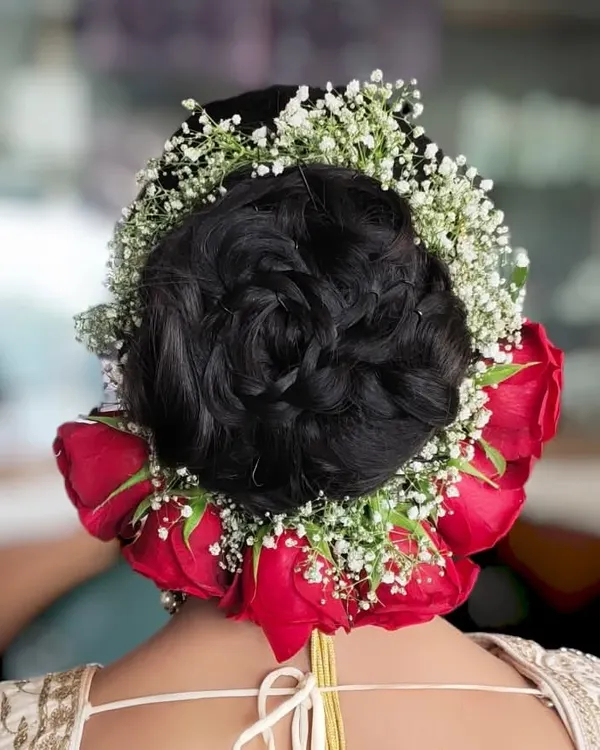 A classic bridal bun, beautifully decorated with a circle of fresh red roses and baby's breath. This is a timeless choice for any wedding ceremony.