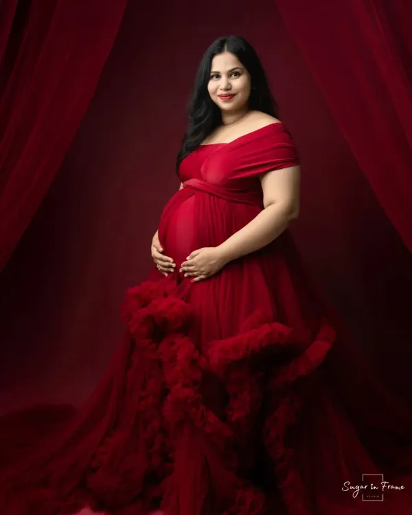 A stunning solo portrait featuring one of our elegant maternity gowns. The rich red color and ruffled details of the dress make for a truly memorable and glamorous shot.