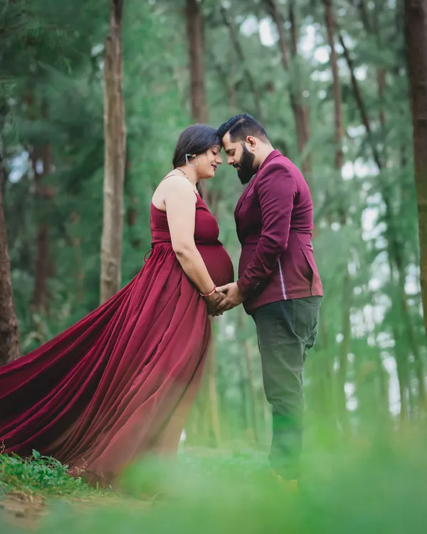 An intimate portrait of an expecting couple in a beautiful forest setting. The flowing red gown adds a touch of drama and elegance to the natural surroundings.