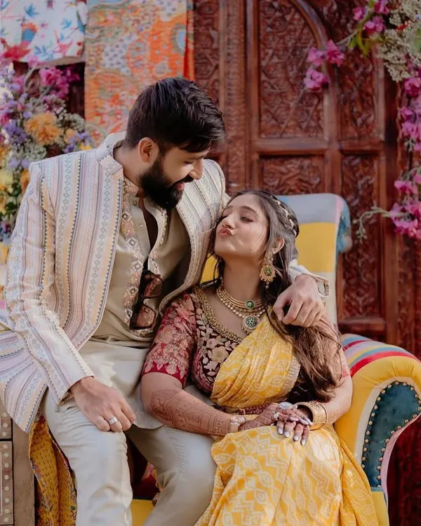 A candid moment of the happy couple at their 'Rajasthani Folklore' Mehendi. The colorful patchwork chair and floral backdrop created a picture-perfect setting.