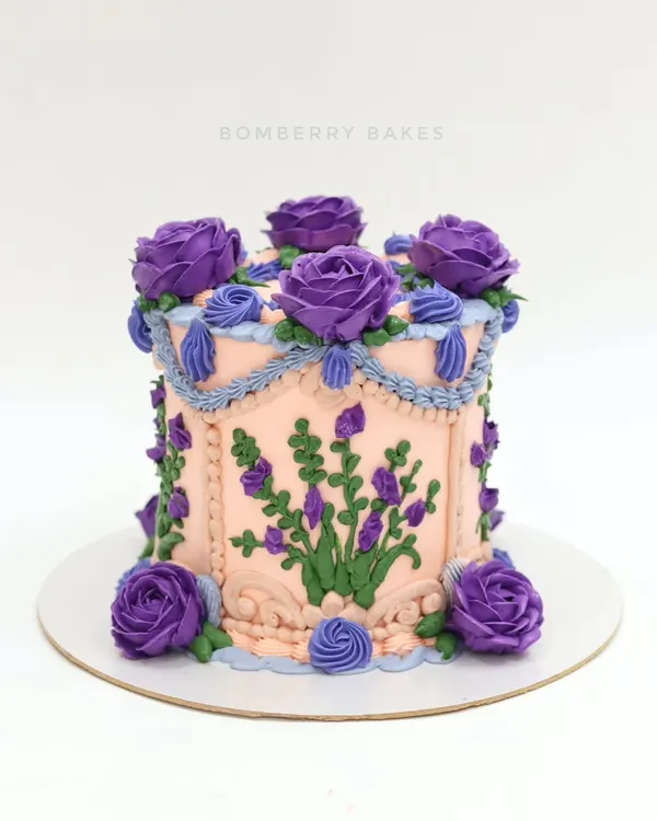 A beautiful vintage-style buttercream cake with a peach base and intricate purple floral piping. This Lambeth-style cake is a timeless classic.