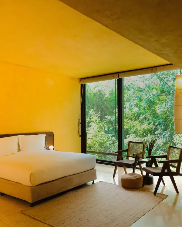 The main bedroom of the Banyan Suite, where minimalist design and natural materials create a calming atmosphere, with the entire wall opening up to a view of the forest.