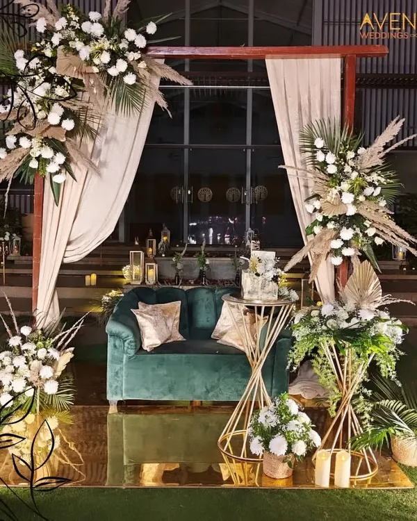We specialize in creating breathtaking focal points for your celebration. This elegant stage combines lush pampas grass, white florals, and a luxurious velvet sofa, all set against a warm, reflective backdrop to create a modern and romantic setting for a wedding reception.
