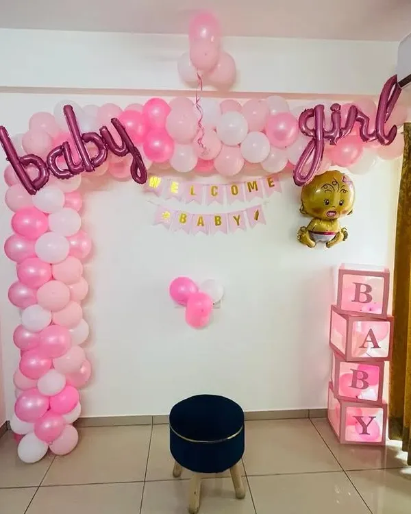 This is a classic "baby girl" welcome home decoration. It features a pink and white balloon arch, "baby girl" foil letters, a "Welcome Baby" banner, and illuminated "BABY" display boxes. It creates a perfect corner for photos.