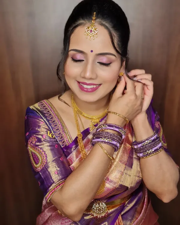 A lovely candid moment of Aparna adjusting her earring. This pose highlights her elegant hairstyle, the maang tikka, and the flawless finish of her makeup.