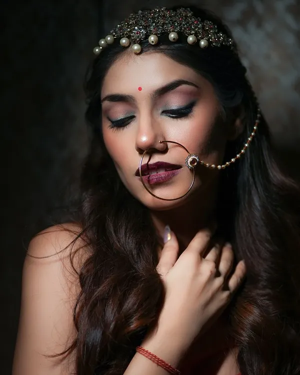 An elegant close-up from an Indian bridal-style shoot. The focus is on the intricate jewelry, like the nath and matha patti, and the soft, expressive makeup, creating a timeless and beautiful portrait.