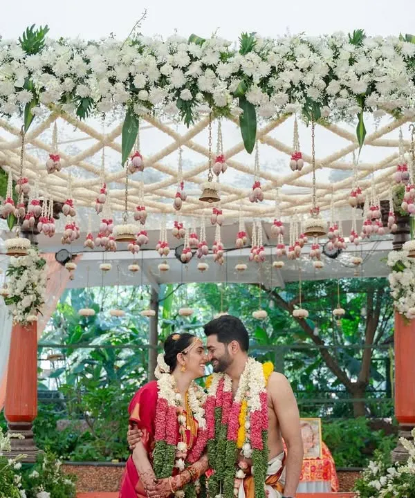 We believe in creating picture-perfect moments. Here, the couple shares a quiet moment under a custom-designed mandap, rich with fresh white orchids and traditional hanging bells, embodying the blend of intimacy and grandeur we strive for in our South Indian wedding designs.